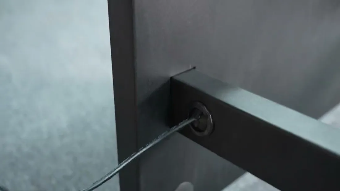 Close-up of a black power cable passing through a grommeted round opening in the horizontal member at the base of the bracket rail.