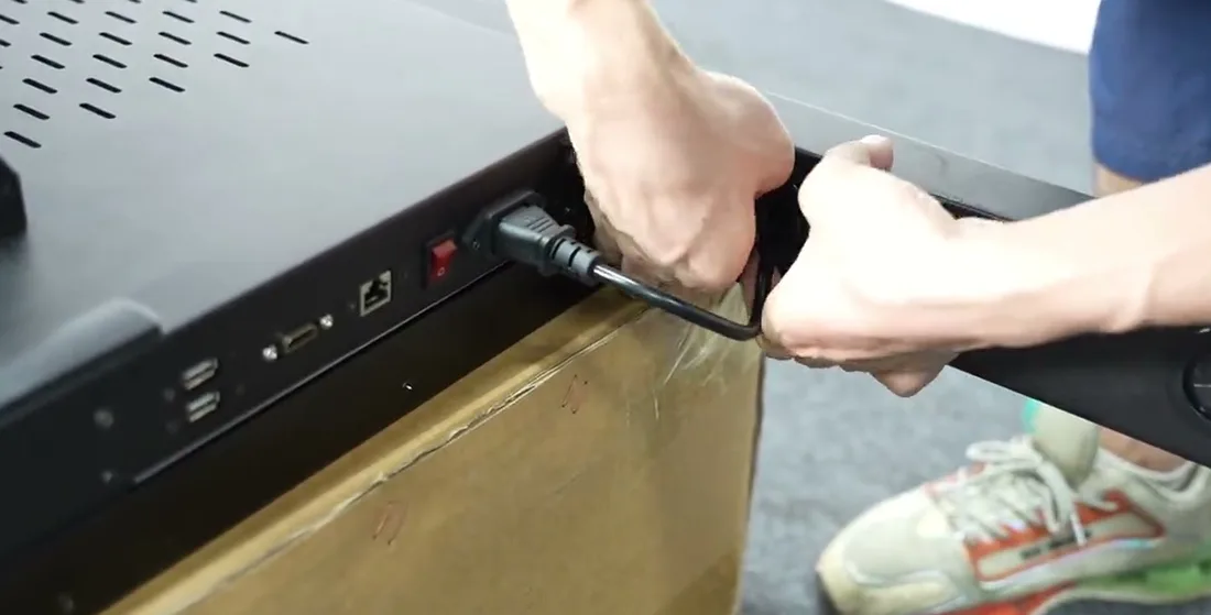The connection panel on the underside edge of the display: USB ports, an HDMI port, a network socket, a red rocker power switch and the power inlet with a cable being plugged in.